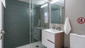 A modern bathroom with a glass shower enclosure, a white sink, and a wooden vanity. - Cloudwalk 1- BR Apartment in Larnaca (Larnaca)