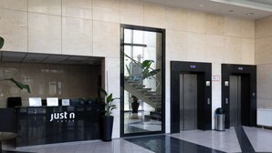 Un área de recepción con un mostrador 'Just N Enter', una escalera y dos ascensores.