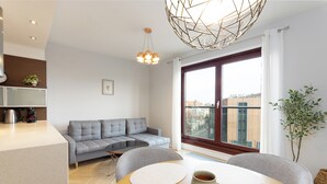 Una sala de estar moderna con un sofá gris, una mesa de comedor con individuales, una cafetera y un amplio ventanal con vista a edificios.
