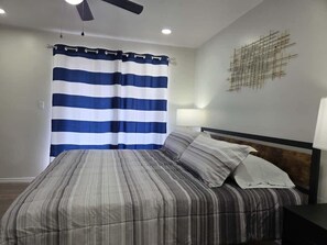 Ein Schlafzimmer mit einem Bett, einem Deckenventilator, einer Wandlampe und einem Streifenvorhang.