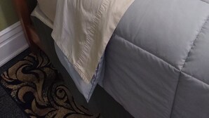 A bed with a wooden headboard, white and gray bedding, and a patterned rug.