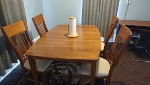 A dining table with four wooden chairs, a spool of white thread, and a power outlet on the wall.