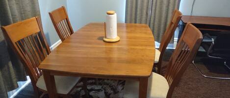 A dining table with four wooden chairs, a spool of white thread, and a power outlet on the wall.