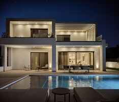 Uma casa moderna de dois andares com piscina, área de estar ao ar livre e um pátio bem iluminado.