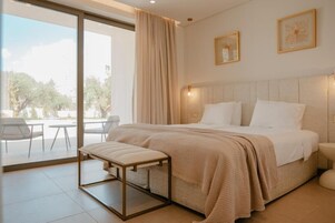 Quarto de hotel moderno com uma cama grande, um banco e vista para o exterior.