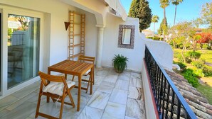A balcony with a wooden table and chairs, a potted plant, and a view of the garden. - Patio Alcornocal by Residea (El Paraíso)