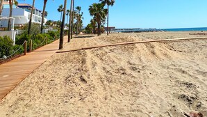 A sandy beach with palm trees and a wooden walkway. - Patio Alcornocal by Residea (El Paraíso)