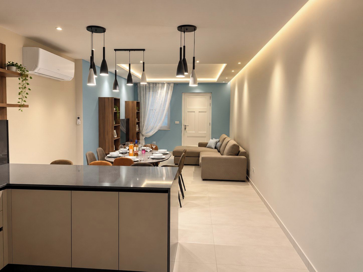 A modern kitchen with a central island, dining area with a table set for four, and a living room with a sofa and a television.
