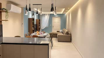 A modern kitchen with a central island, dining area with a table set for four, and a living room with a sofa and a television.