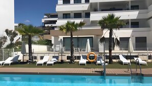 A modern building with a pool area, including lounge chairs and umbrellas.
