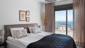 A bedroom with a bed, a nightstand, a lamp, a view of the city, and a window with curtains.