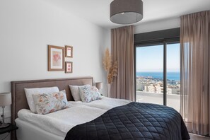 A bedroom with a bed, a nightstand, a lamp, a view of the city, and a window with curtains.