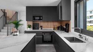 A modern kitchen with dark cabinetry, a built-in oven, a sink, and a window with a view of buildings.