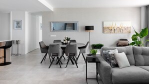A modern living room with a grey sofa, a dining table with chairs, a floor lamp, and a large mirror on the wall.