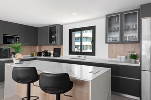A modern kitchen with dark cabinets, a marble island, two black bar stools, and a large window.