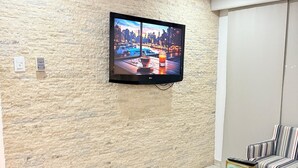 A modern living room with a flat-screen TV mounted on a textured wall, striped sofas, a glass coffee table, and a remote control on a wooden block. - Beautiful apartment (Porlamar)