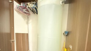 A compact room with a large cylindrical tank, wooden wardrobe, and a small shelf with various items. - Beautiful apartment (Porlamar)