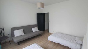 Habitación minimalista con un sofá gris, una mesita pequeña y una cama individual.