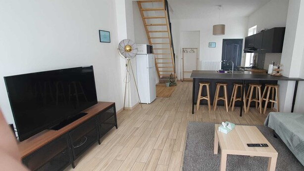 Una sala moderna con televisor de pantalla plana, un sofá, una mesa de centro y una zona de cocina con un taburete de bar.