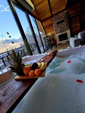 Ein Wellnessbereich mit Whirlpool, einem Holztisch mit Früchten und Kerzen sowie Blick auf die Stadt durch große Fenster.