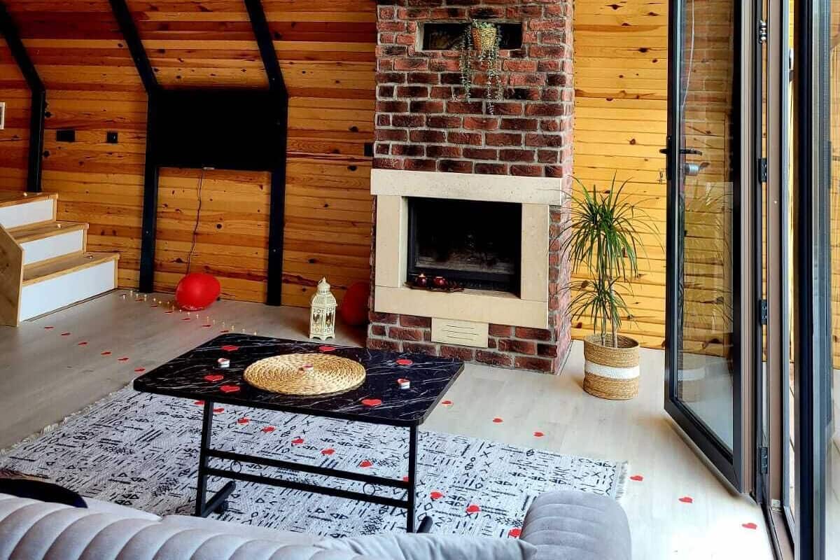 Een gezellige woonkamer met een metselaarsschouw, houten balken, een trap en een groot raam.