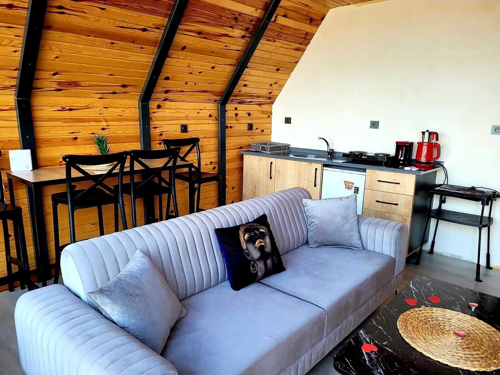A cozy loft-style living space with a high ceiling, a sofa with a pillow, a dining table with chairs, and a kitchenette.