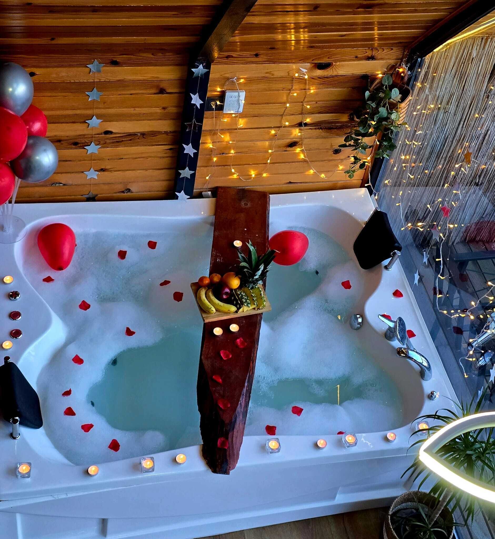 Une baignoire remplie de pétales de rose, avec des bougies et des fruits.