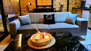 Une pièce chaleureuse avec un canapé gris, une petite table ornée de bougies et un plafond en bois.