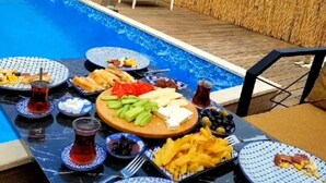 Un espace de restauration aménagé au bord de la piscine, avec une table dressée pour un repas, entouré d’une terrasse en bois et offrant une vue sur les montagnes.