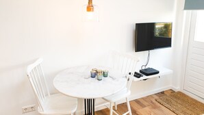 Un comedor con mesa redonda, sillas blancas, una lámpara colgante y un televisor montado en la pared.