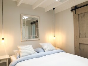 A bedroom with a bed, two bedside tables, a mirror, and a wooden door. - Quiet studio near the dunes, close to downtown, with private parking.   (Zandvoort)