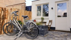 Una bicicleta estacionada junto a un muro de ladrillo, una puerta blanca y una ventana con vista a los árboles.