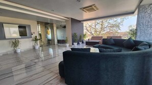 Una sala de estar moderna con un sofá oscuro, una mesa de centro y plantas en macetas. Una ventana grande ofrece luz natural y vistas a árboles.
