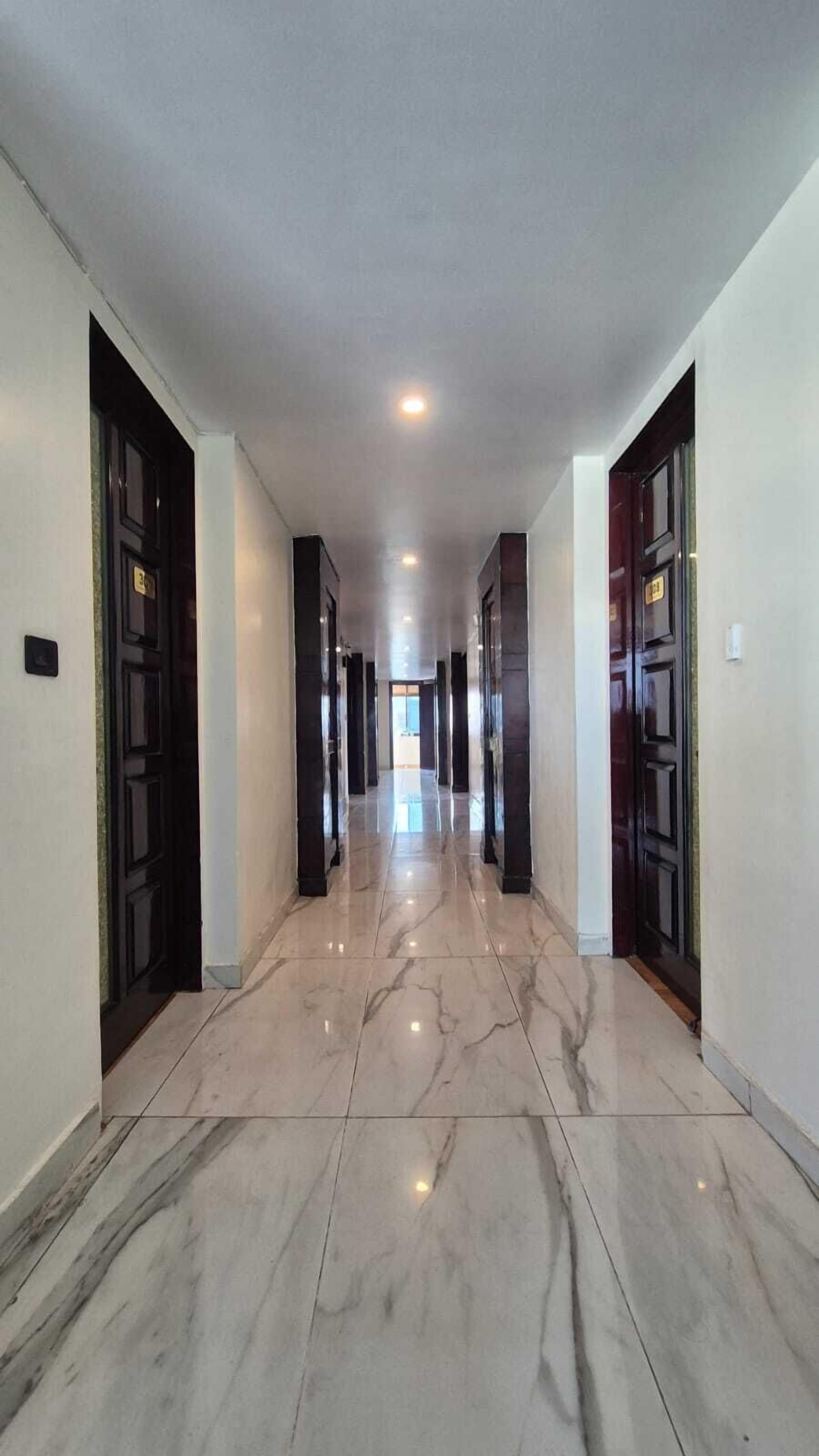 A long, narrow hallway with marble flooring and dark wooden doors on both sides.