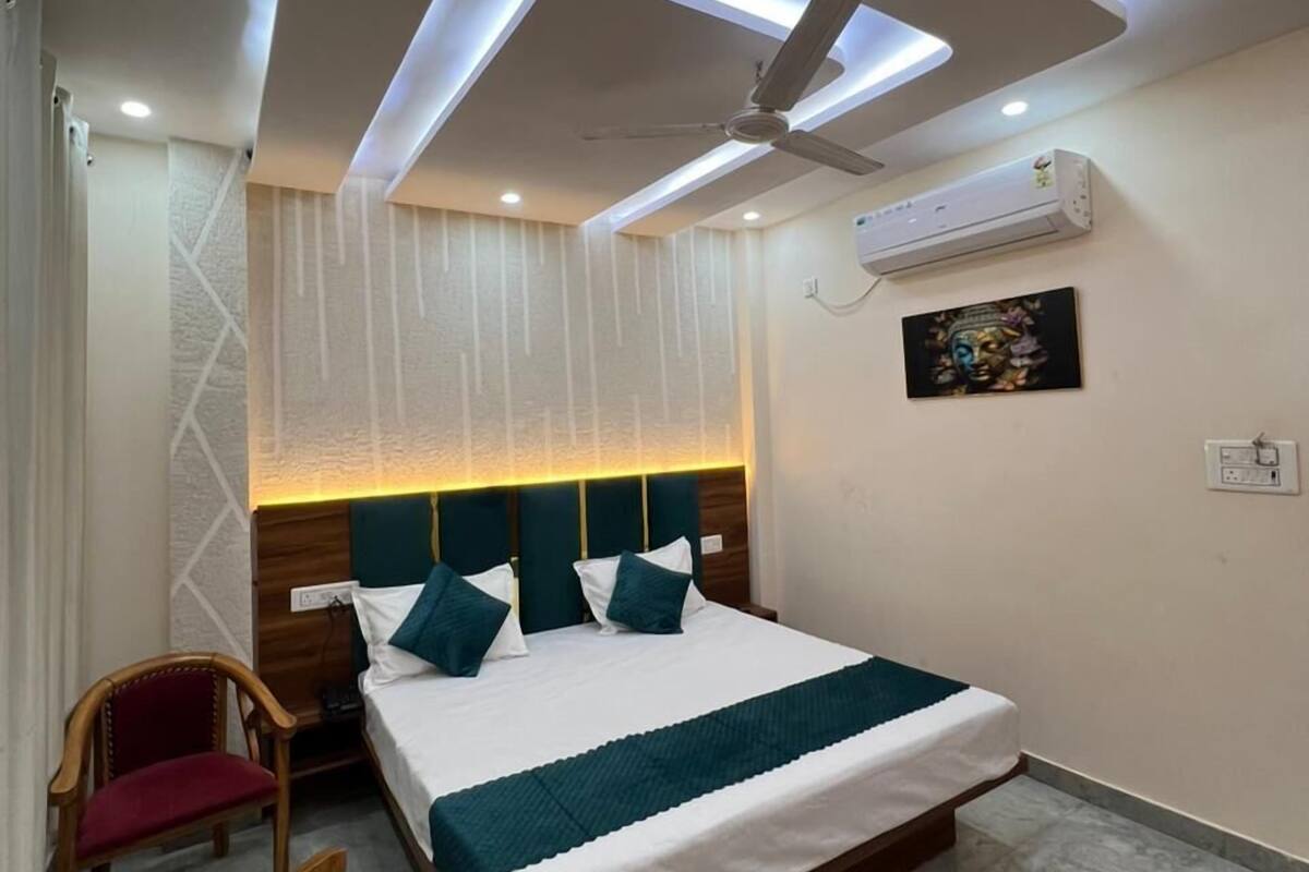 Habitación de hotel con cama, ventilador de techo, iluminación empotrada, aire acondicionado y un cuadro colgado en la pared.