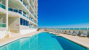 A pool area with a clear blue pool, white poolside chairs, and a building with balconies. - Silver Beach 806 | Top Floor, Corner, Beach Front - Penthouse Upgrades! (Orange Beach)