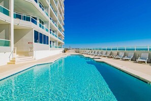A pool area with a clear blue pool, white poolside chairs, and a building with balconies. - Silver Beach 806 | Top Floor, Corner, Beach Front - Penthouse Upgrades! (Orange Beach)