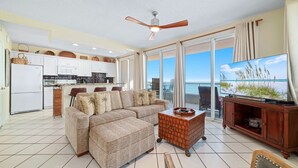 A spacious living room with a large sofa, a television, and a balcony with a view of the ocean. - Silver Beach 806 | Top Floor, Corner, Beach Front - Penthouse Upgrades! (Orange Beach)