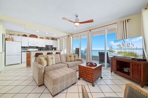 A spacious living room with a large sofa, a television, and a balcony with a view of the ocean. - Silver Beach 806 | Top Floor, Corner, Beach Front - Penthouse Upgrades! (Orange Beach)