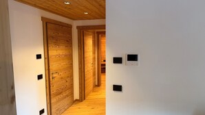 A hallway with wooden flooring, a wooden door, and a white wall with several small black square objects. - Apartment 'Stella' with Mountain View, Private Terrace and Wi-Fi (Isolaccia)