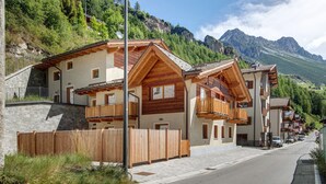 A row of wooden buildings with balconies, set against a mountainous backdrop. - Apartment 'Stella' with Mountain View, Private Terrace and Wi-Fi (Isolaccia)