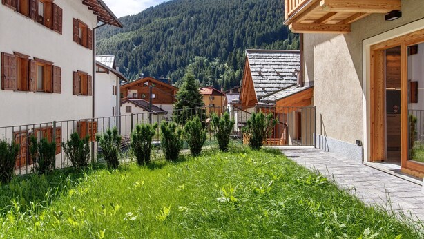 A courtyard with a stone pathway, wooden buildings with shutters, and a mountainous backdrop. - Apartment 'Stella' with Mountain View, Private Terrace and Wi-Fi (Isolaccia)