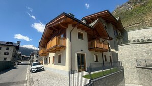 A two-story building with wooden balconies, a paved street, and a mountain in the background. - Apartment 'Stella' with Mountain View, Private Terrace and Wi-Fi (Isolaccia)