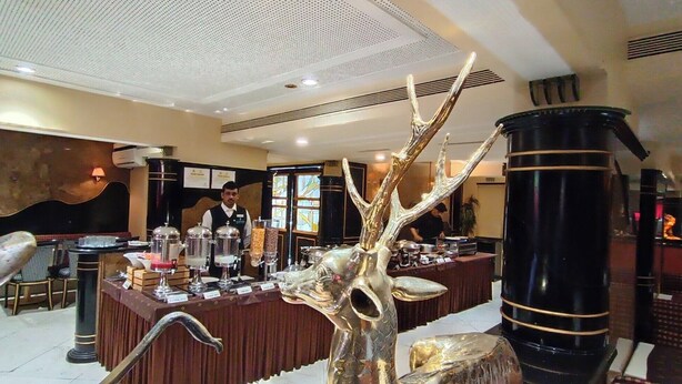 A hotel lobby with a reception desk, a large decorative sculpture, and a seating area. - Rajhans Hotel (Mumbai)