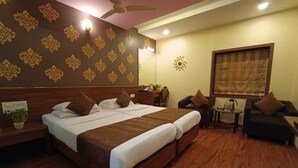 A hotel room with a large bed, a desk, a chair, and a small table with a lamp. - Rajhans Hotel (Mumbai)
