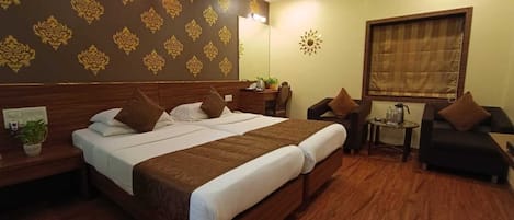 A hotel room with a large bed, a desk, a chair, and a small table with a lamp.