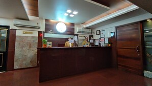 A reception desk with a clock, a sign for a restaurant, and a potted plant. - Rajhans Hotel (Mumbai)