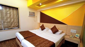 A hotel room with a large bed, wooden headboard, and a bedside table with a phone and a small box. - Rajhans Hotel (Mumbai)