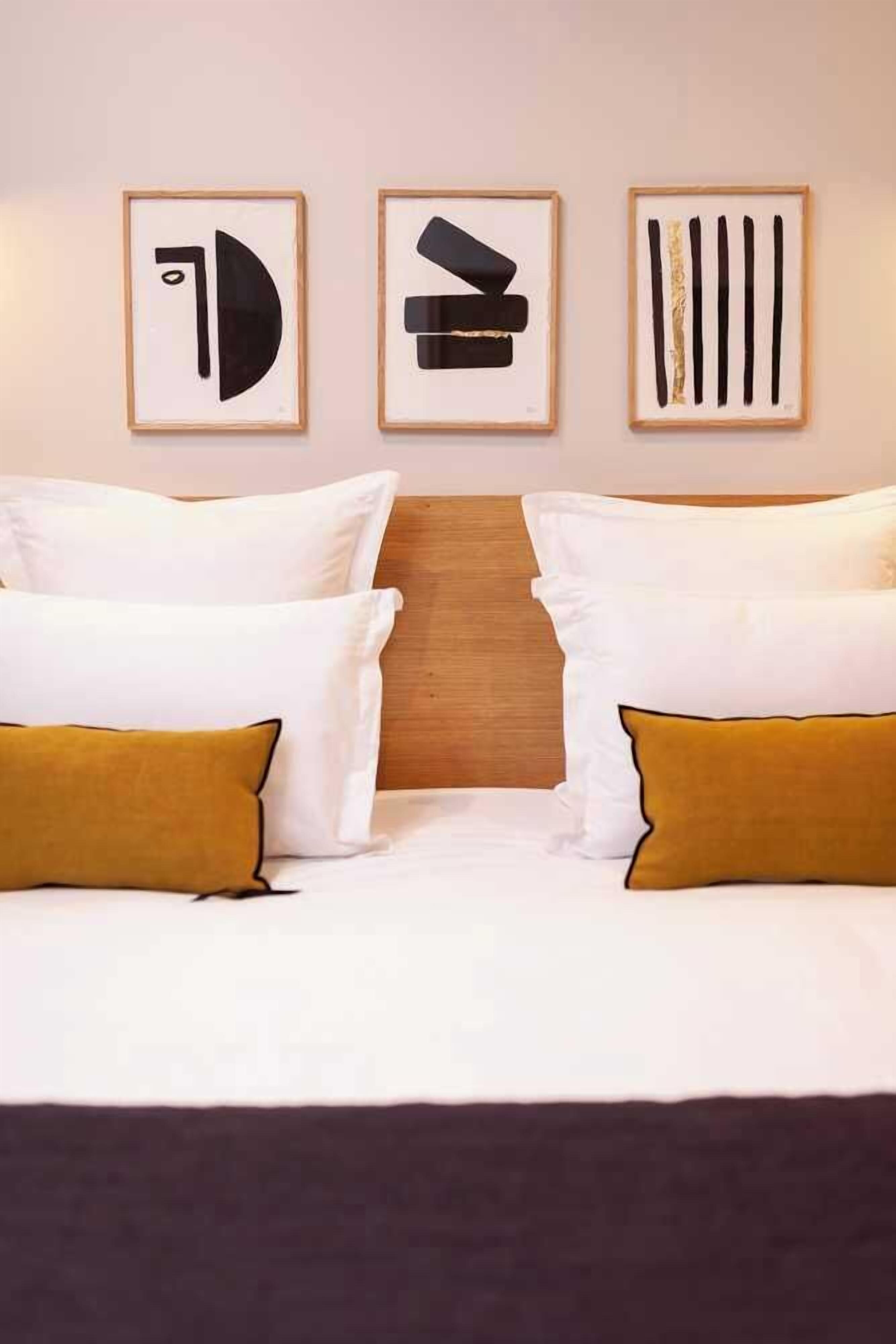 Habitació d'hotel amb un llit, dues almoines i tres quadres al mur.