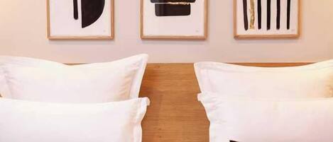 A hotel room with a bed, two pillows, and three framed artworks on the wall.